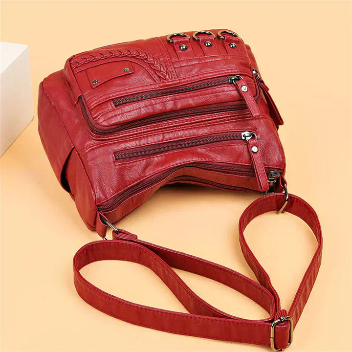 Red leather crossbody bag close-up with layered zipper pockets and adjustable strap