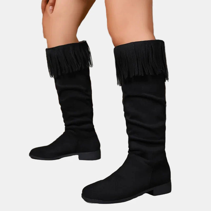 Black knee-high tassel boots with fringed cuff and low block heel.