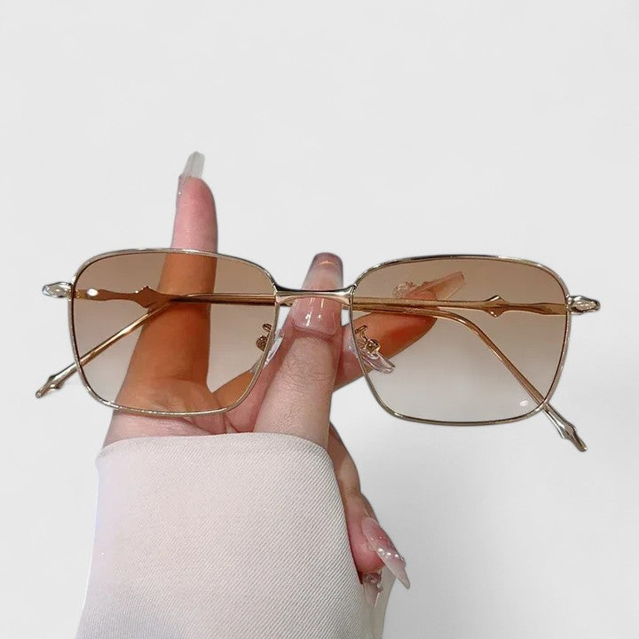 Raygynn sunglasses held in hand with pink-tinted lenses and gold metal frame