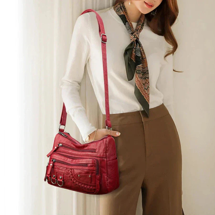 Red crossbody bag on shoulder with multiple front zippers and metal ring details