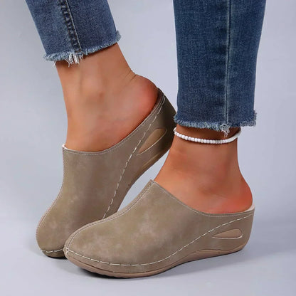 Taupe orthopedic mules on feet with cushioned insole, suede-like upper and stitched seams