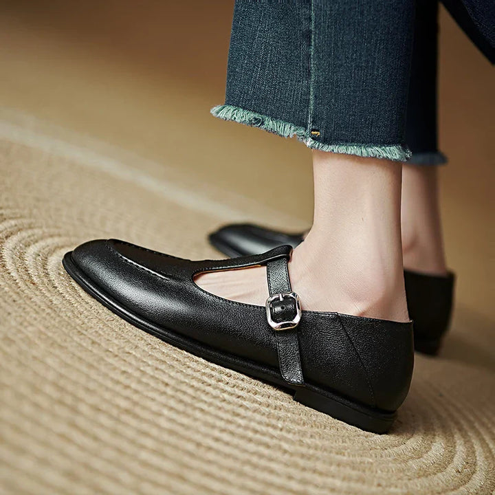 Black low-heeled Mary Jane pumps with T-strap buckle and cutout vamp, back side view.