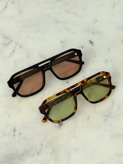 Two sunglasses on a surface: black frames with peach lenses and tortoiseshell with green lenses