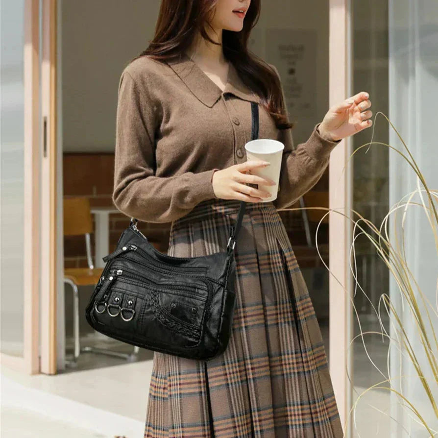 Black multi-layer crossbody bag worn across the body with layered zip compartments