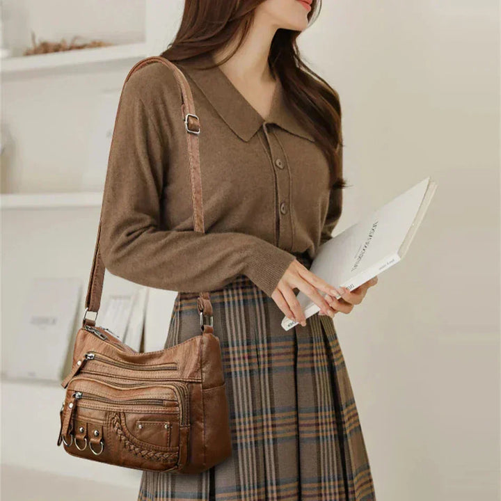 Brown leather crossbody bag worn on shoulder; multi-zip front with braided pocket and ring straps
