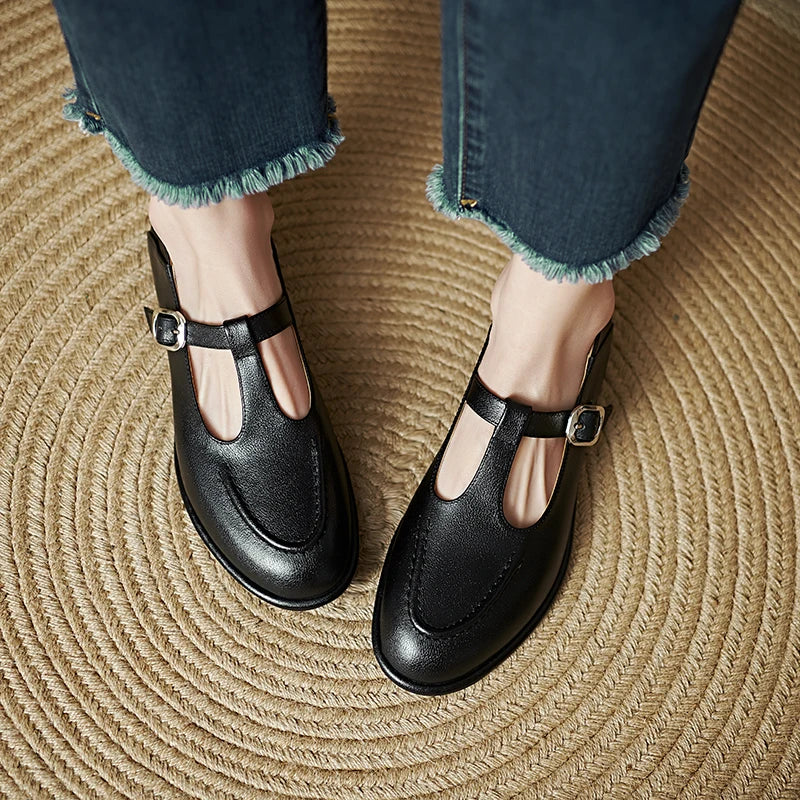 Black low-heeled Mary Jane pumps with T-strap buckle and rounded toe, side view.