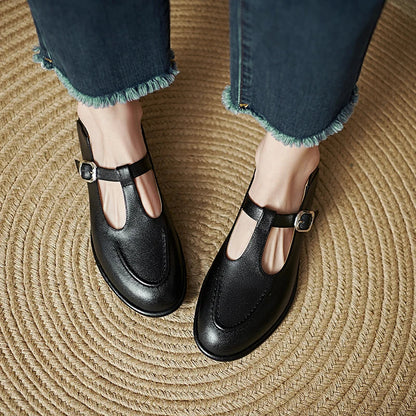 Black low-heeled Mary Jane pumps with T-strap buckle and rounded toe, side view.