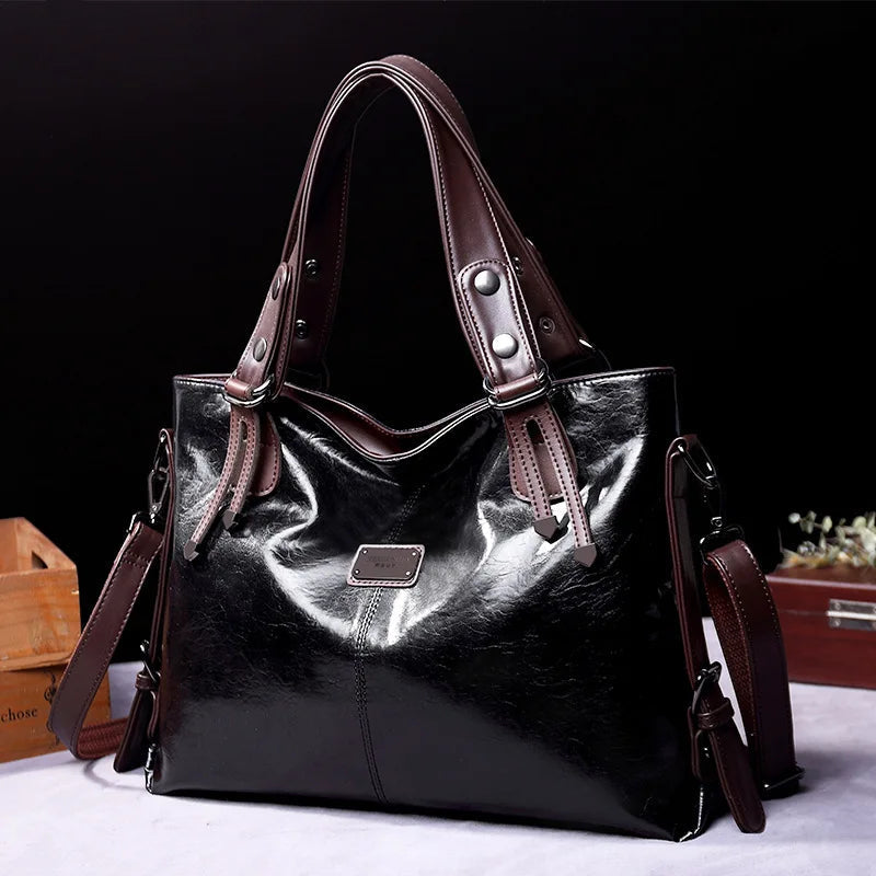 Black soft leather tote bag with double handles, side straps, and front logo patch
