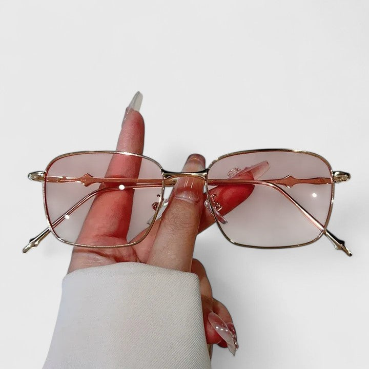 Raygynn sunglasses held in hand with pink-tinted lenses and gold metal frame