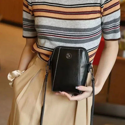 Black mini crossbody handbag with zipper top and sunburst emblem, held in hands.