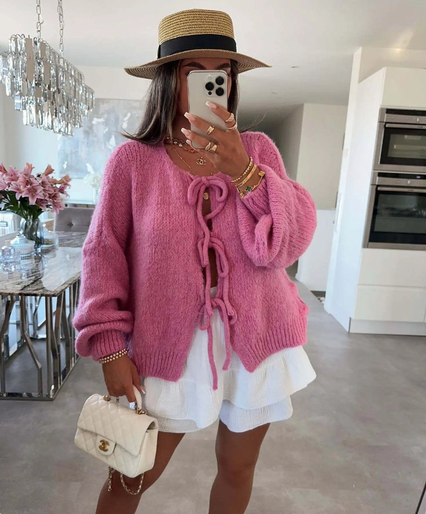 Pink knitted bow cardigan with front bow ties and textured chunky sleeves.