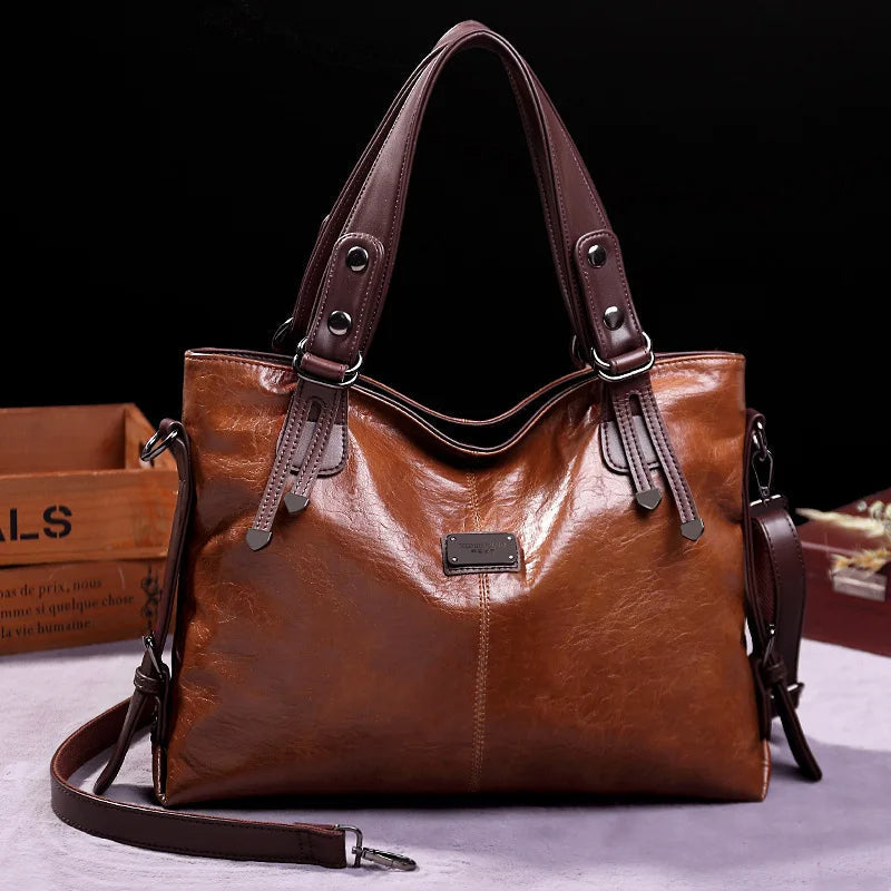 Brown soft leather tote bag with double handles, front logo patch, and crossbody strap