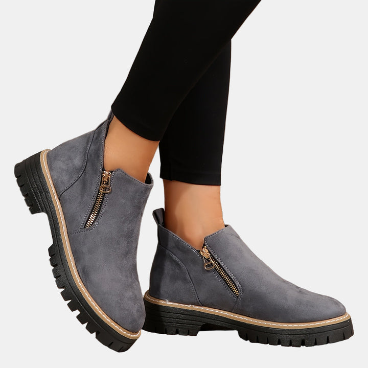 Gray suede ankle boots with side zipper and tan-stitched welt, chunky lug sole.