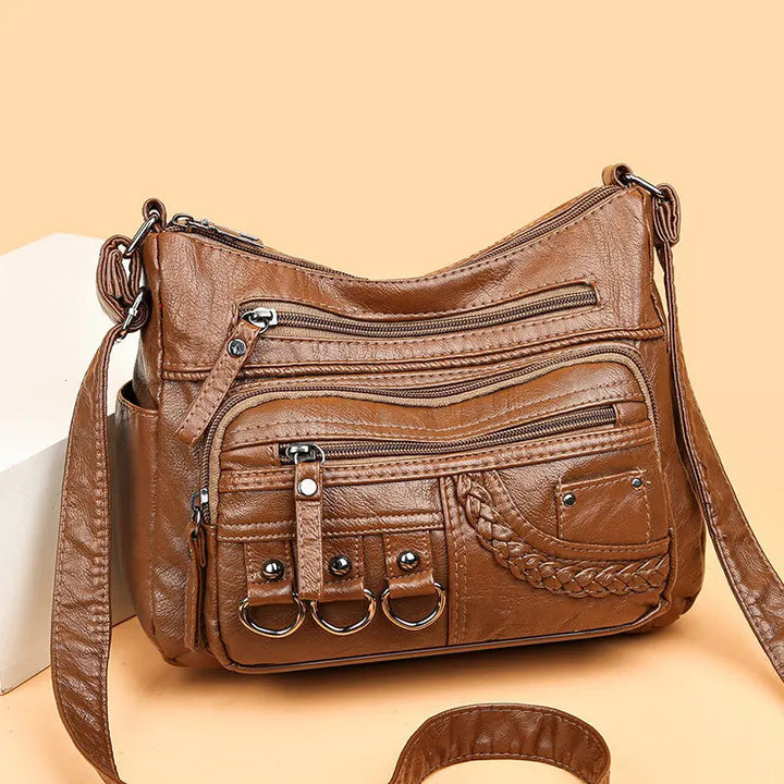 Brown multi-layer crossbody bag with double strap, zip pockets, braided front panel, and metal rings