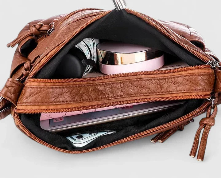 Women’s brown leather shoulder bag interior shown with slots and a phone-like device.