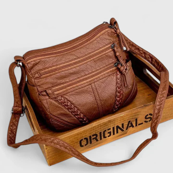 Women’s brown leather crossbody bag with two front zipper compartments and braided trim.
