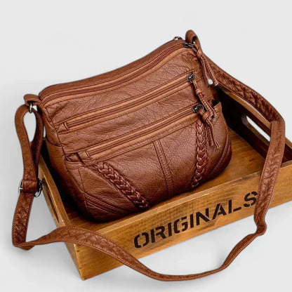 Women’s brown leather crossbody bag with two front zipper compartments and braided trim.