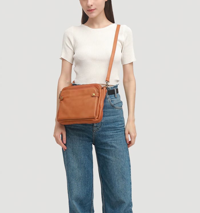 Orange-brown crossbody bag on shoulder with zip front pockets and gold-tone hardware