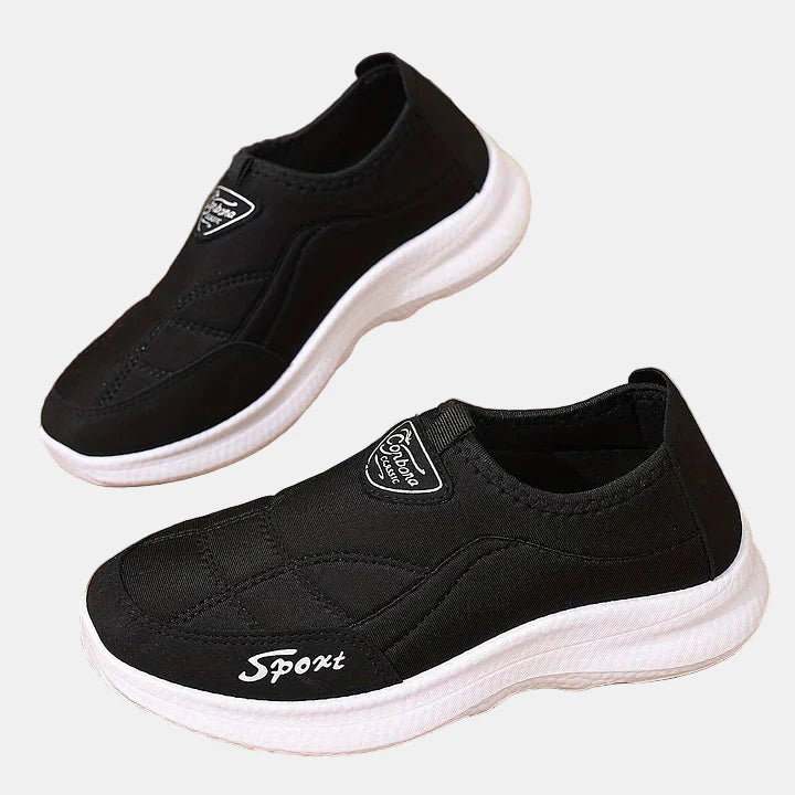Black slip-on sneakers with white rubber sole and logo at side