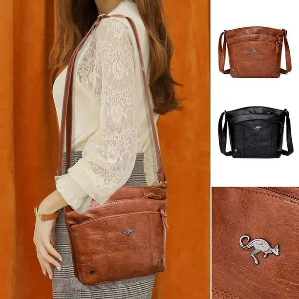 Tan leather crossbody bag on model with long strap, zip top, and front kangaroo logo.