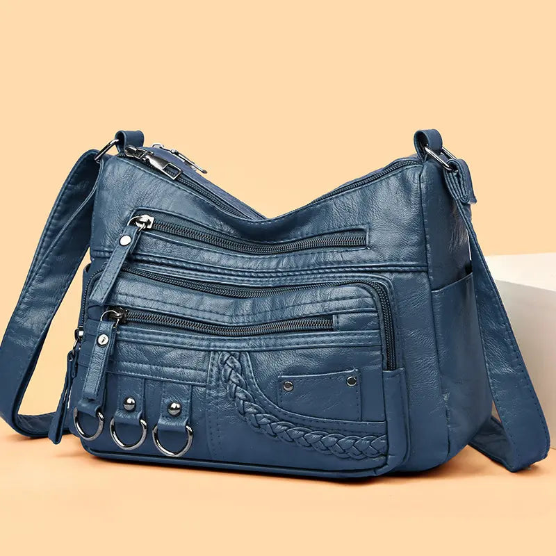 Blue multi-layer crossbody bag with multiple zippers, braided front pocket, and ring pulls