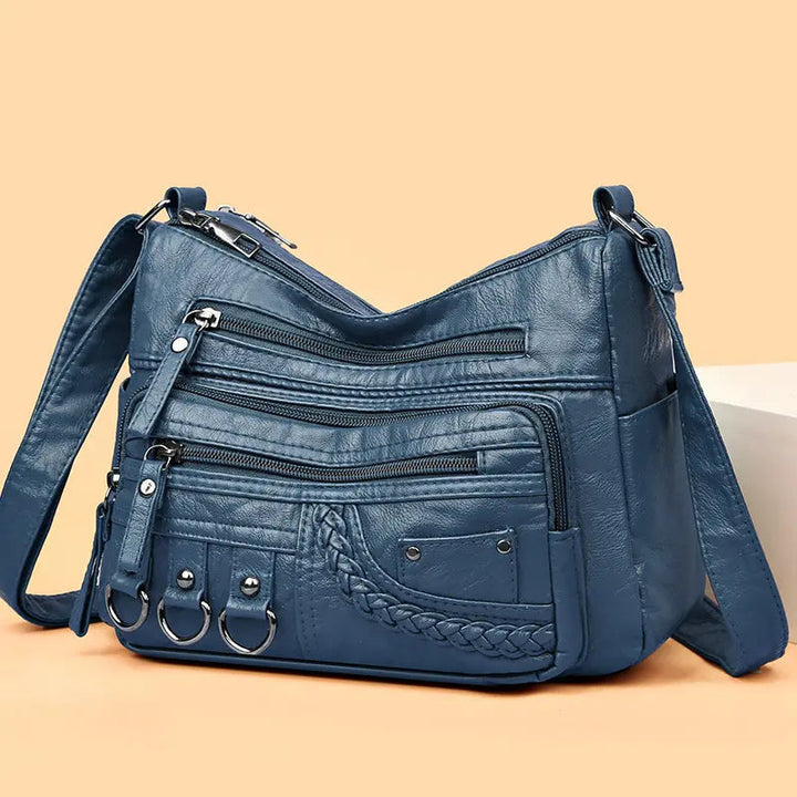 Blue multi-layer crossbody bag with multiple zippers, braided front pocket, and ring pulls