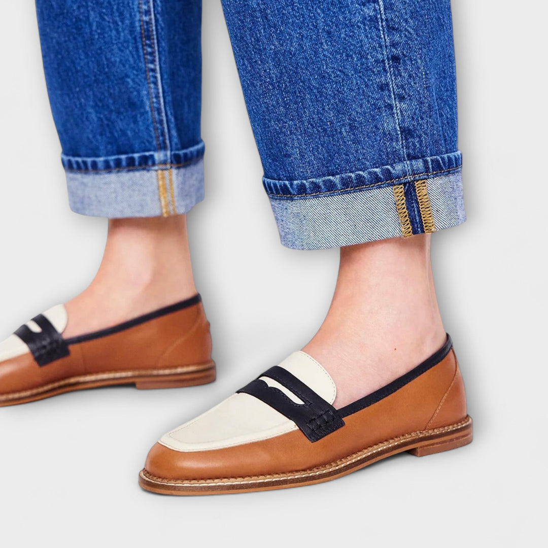 Brown round-toe loafers with white panel and black strap, worn with blue jeans