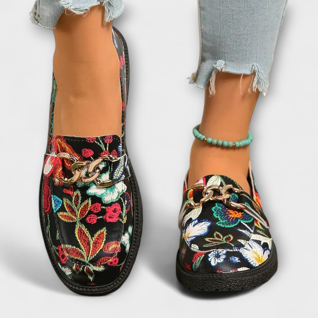 Multicolour floral loafer pair, black slip-on with gold chain buckle and rounded toe