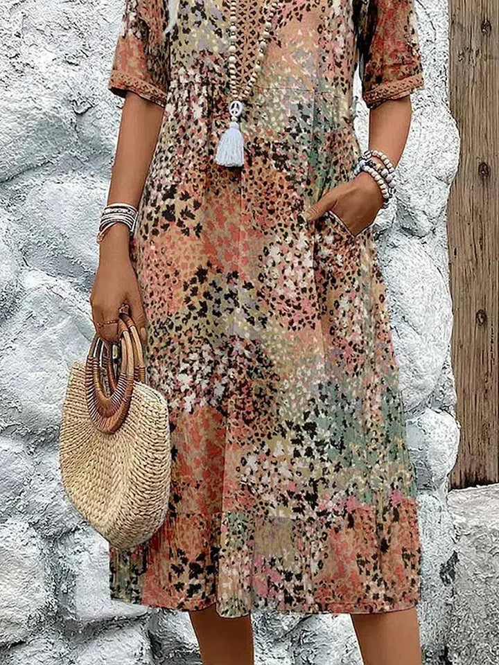 Mid-length V-neck dress hem in sandy beige with multicolor speckled pattern and tassel trim