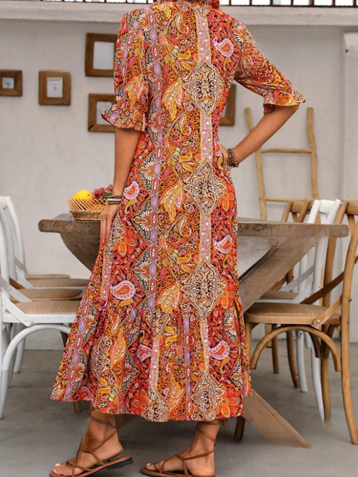 Boho grace dress in orange-red paisley print, close view of tassel-trimmed center and tiered hem