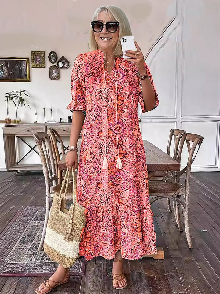 Boho grace dress in orange-red paisley print with tassel neckline, short puff sleeves, tiered skirt