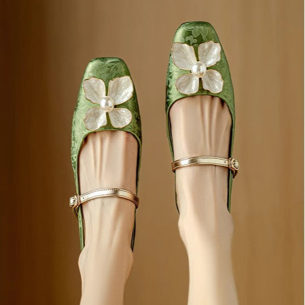 Pair of green pumps with pointed toe, T-strap, and white flower detail at the vamp