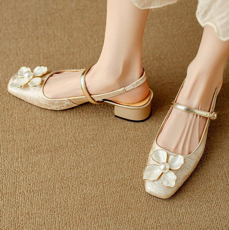 Beige pumps with rounded toe, ankle strap, and white flower on the vamp