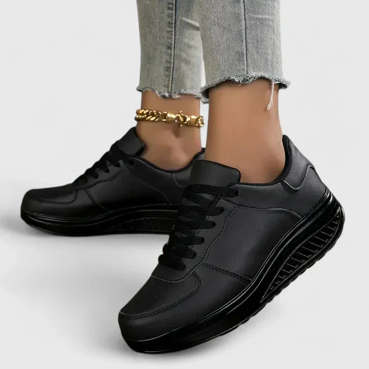 Black orthopedic sneakers, lace-up with dark padded tongue and chunky sole tread.