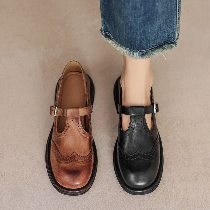 Brown and black leather Mary Jane shoes with buckle straps and wingtip stitching.