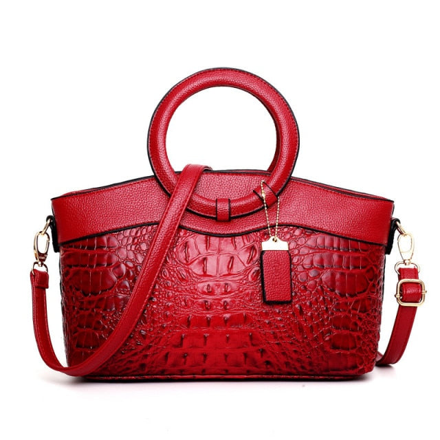 Red croc-textured women’s handbag with top handles and crossbody strap