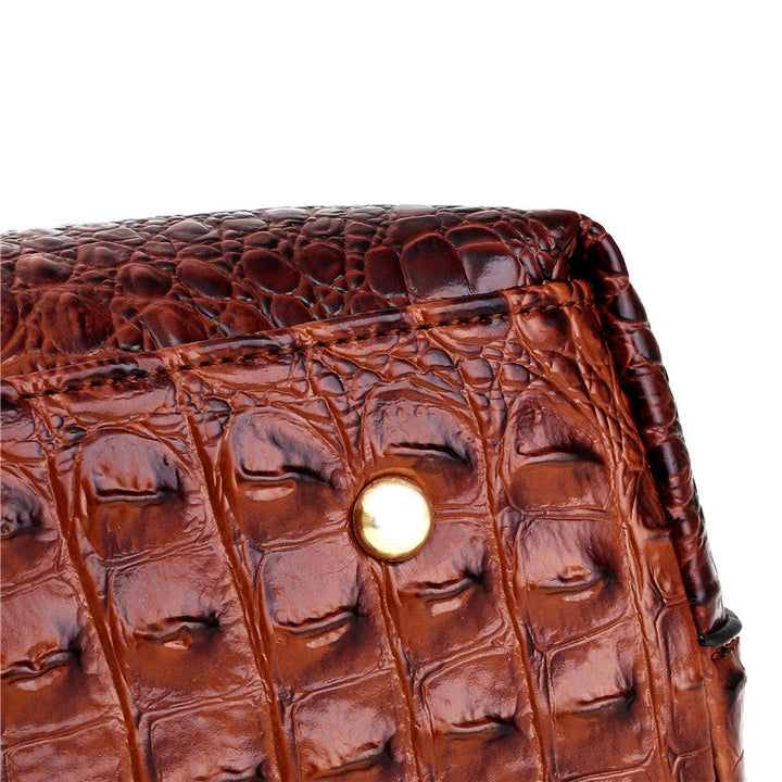 Brown croc-embossed handbag front with gold-tone snap and textured pattern detail.