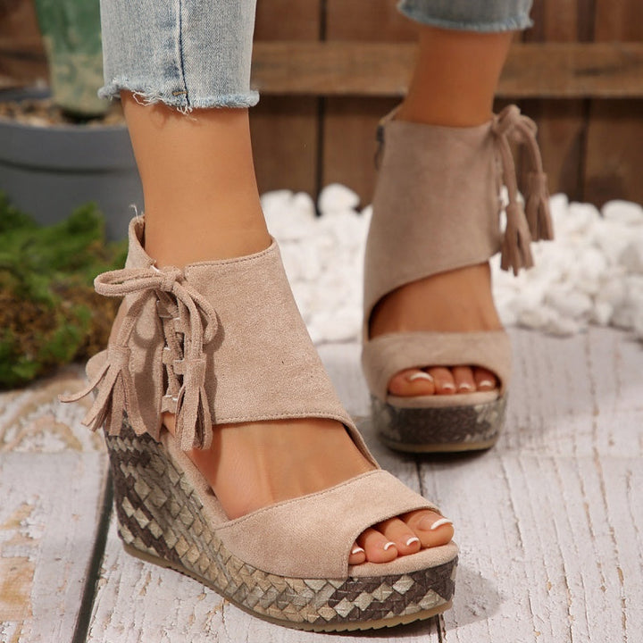 Beige suede wedge sandals with tassel tie straps and peep toe on patterned sole.
