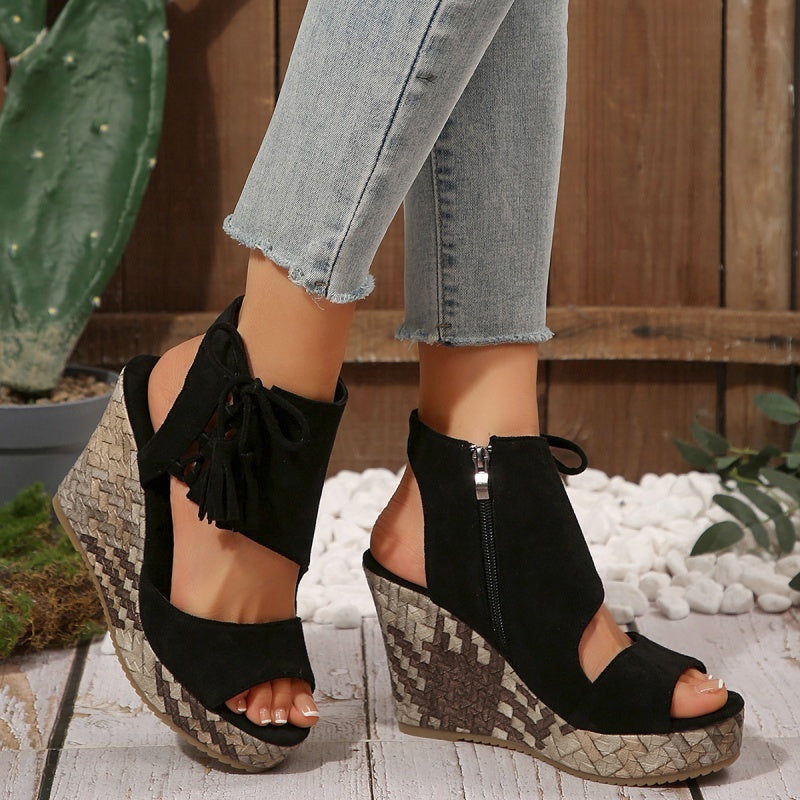 Black suede wedge sandals with open toe, tassel ties, and zip ankle on patterned sole.