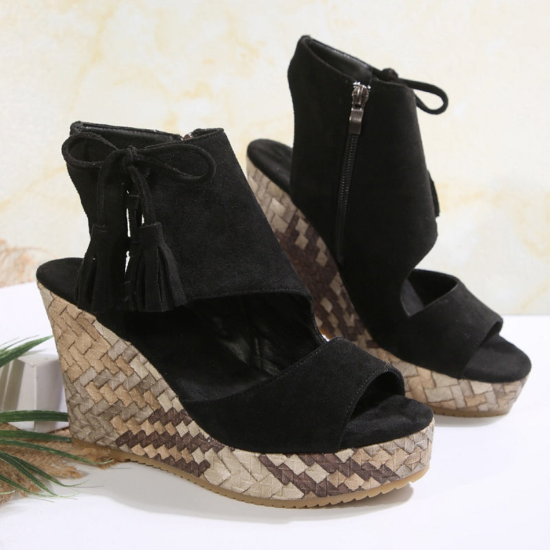 Black suede heeled sandals with open toe, zip ankle, and patterned wedge sole.